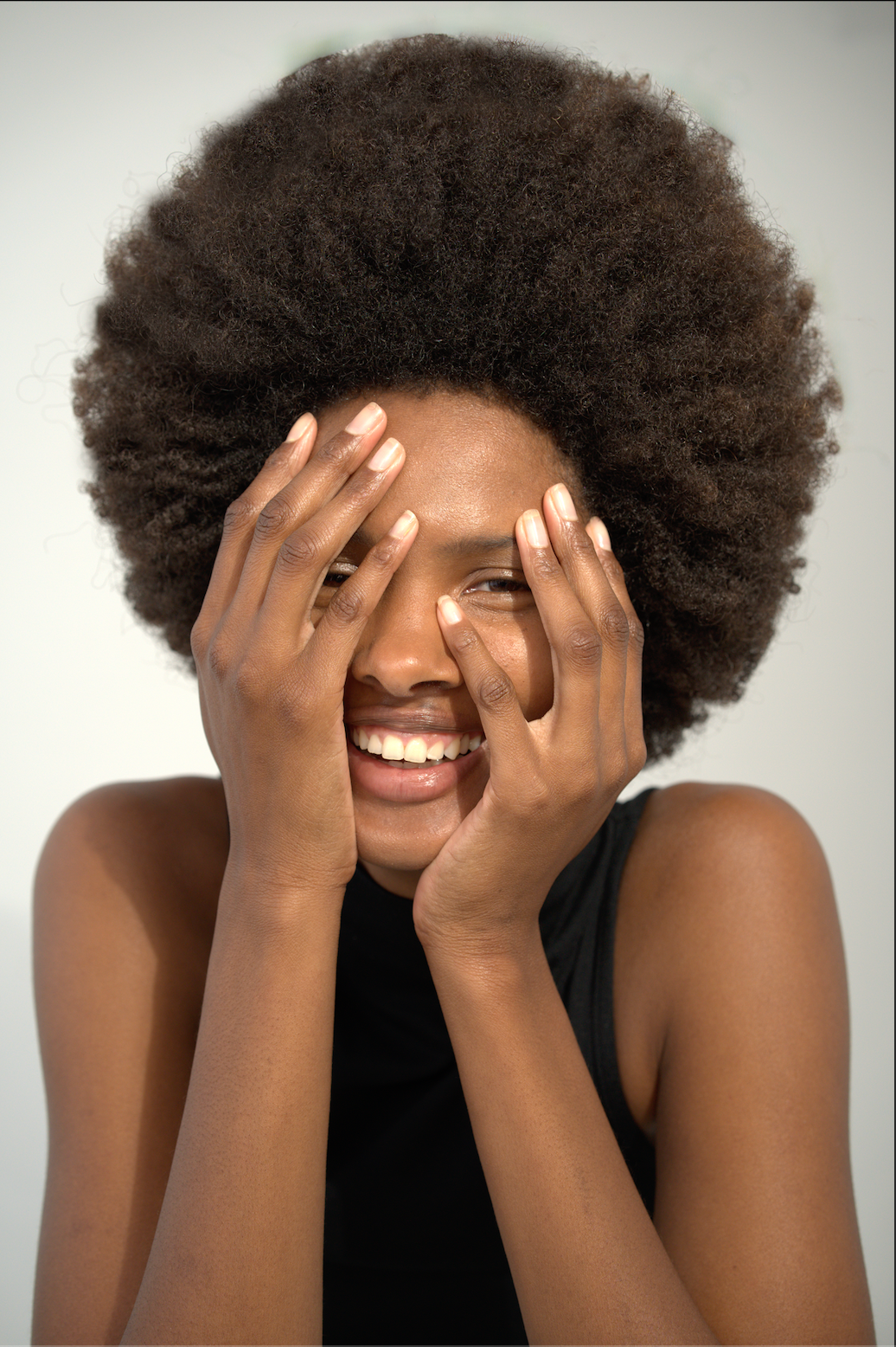 Person with large afro smiling with hands on face