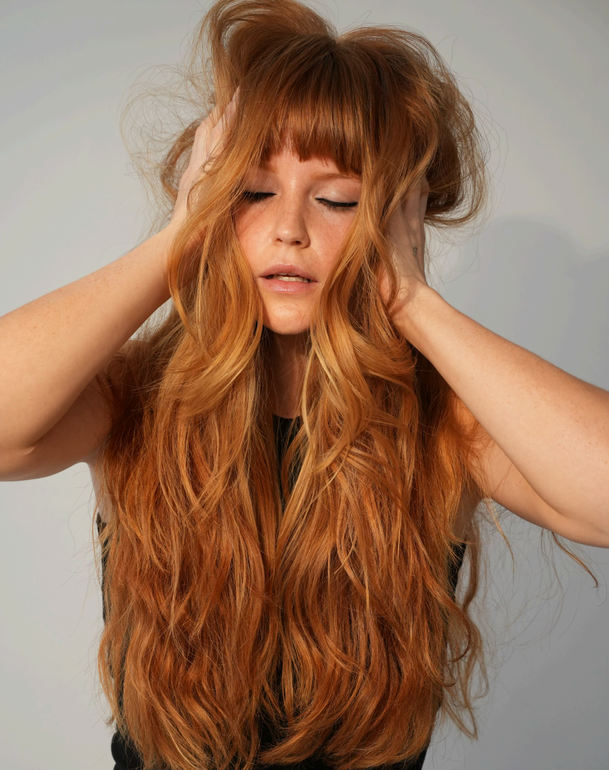 Woman with long, wavy red hair against a plain background